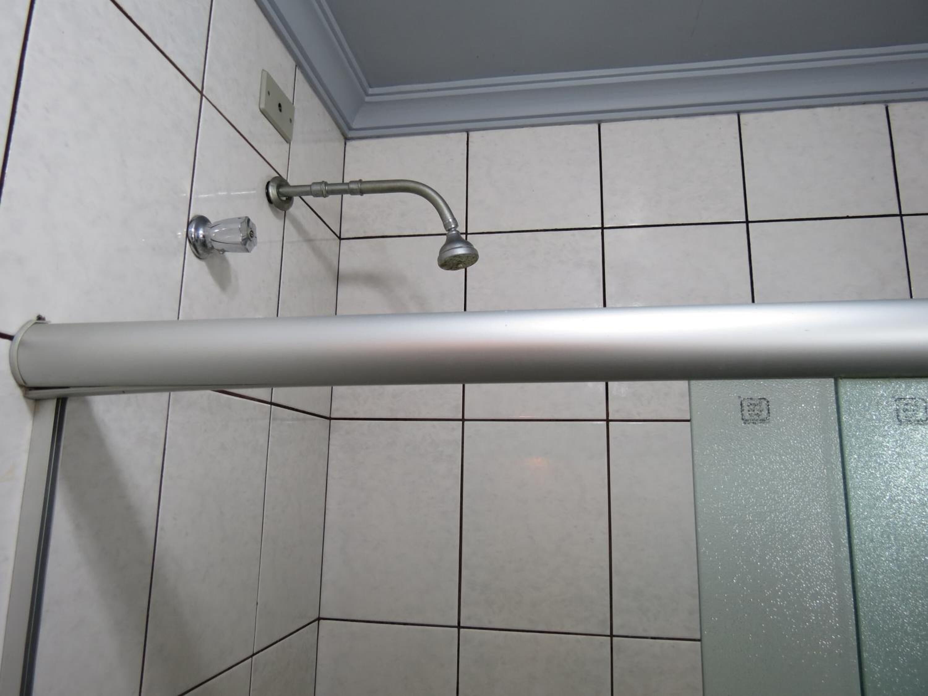 Ein Duschbereich mit einer Metallhandstange, gefliesten Wänden und einer Decke mit einer eingelassenen Leuchte.
