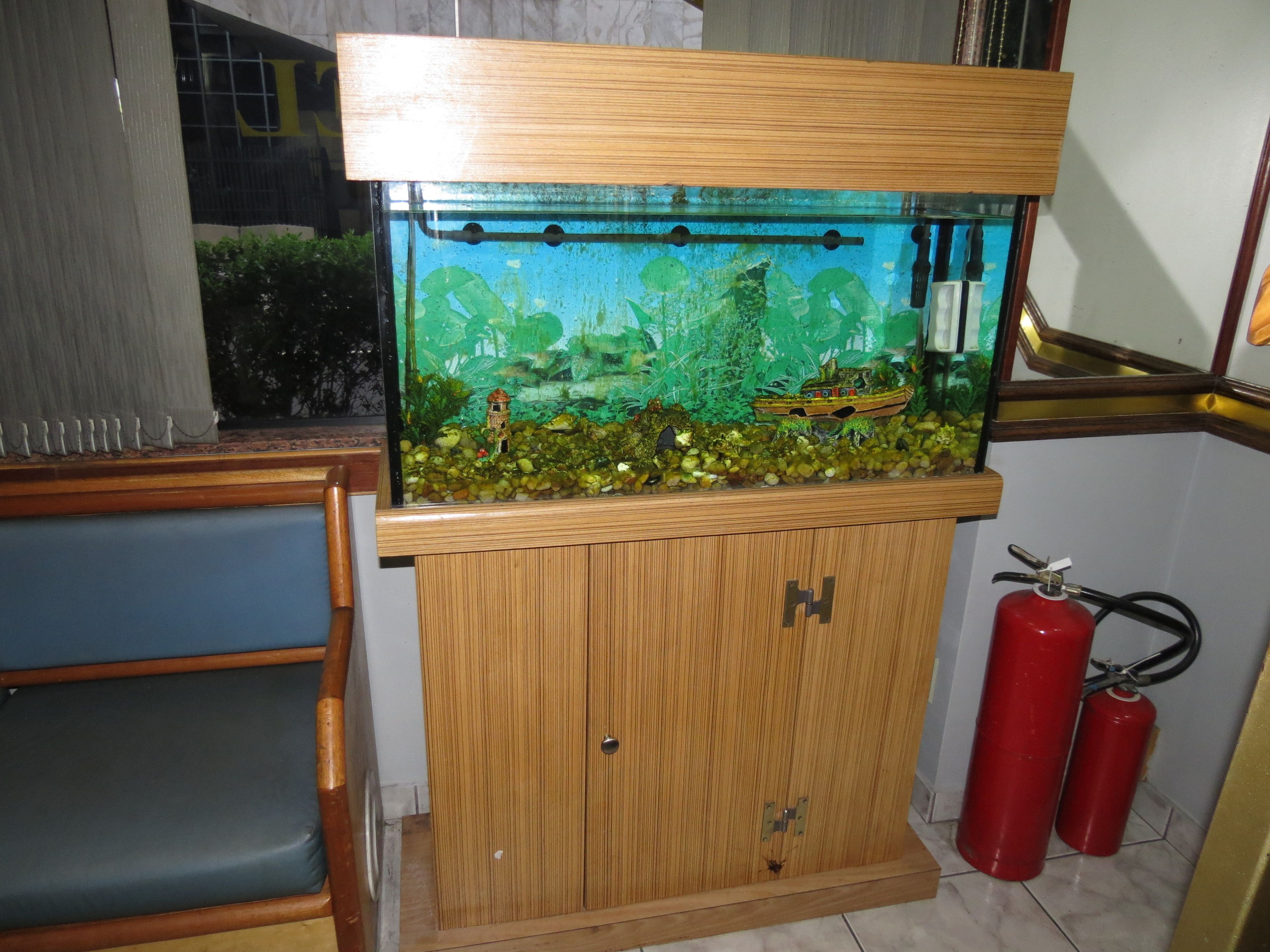 Un acuario con un mueble de madera, un barco pequeño y dos extintores rojos.