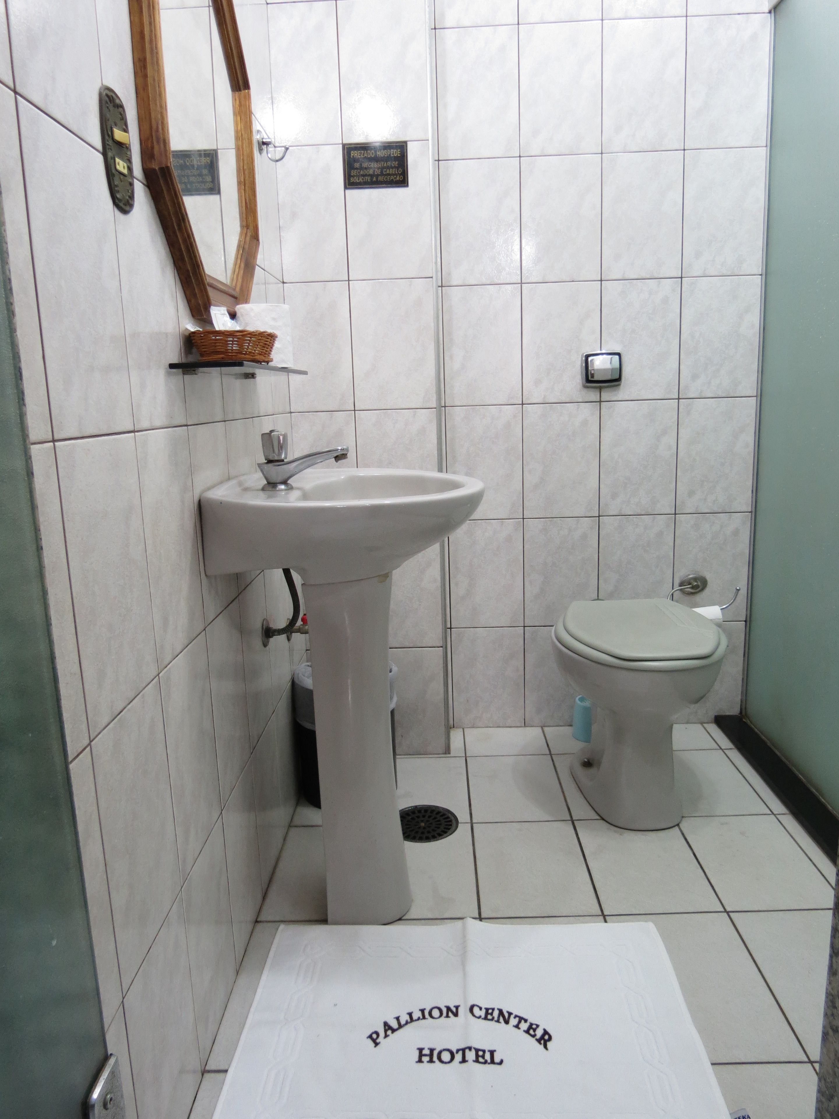 A bathroom with a white sink, a toilet, and a mirror on the wall. There is a sign on the wall and a placard on the floor.