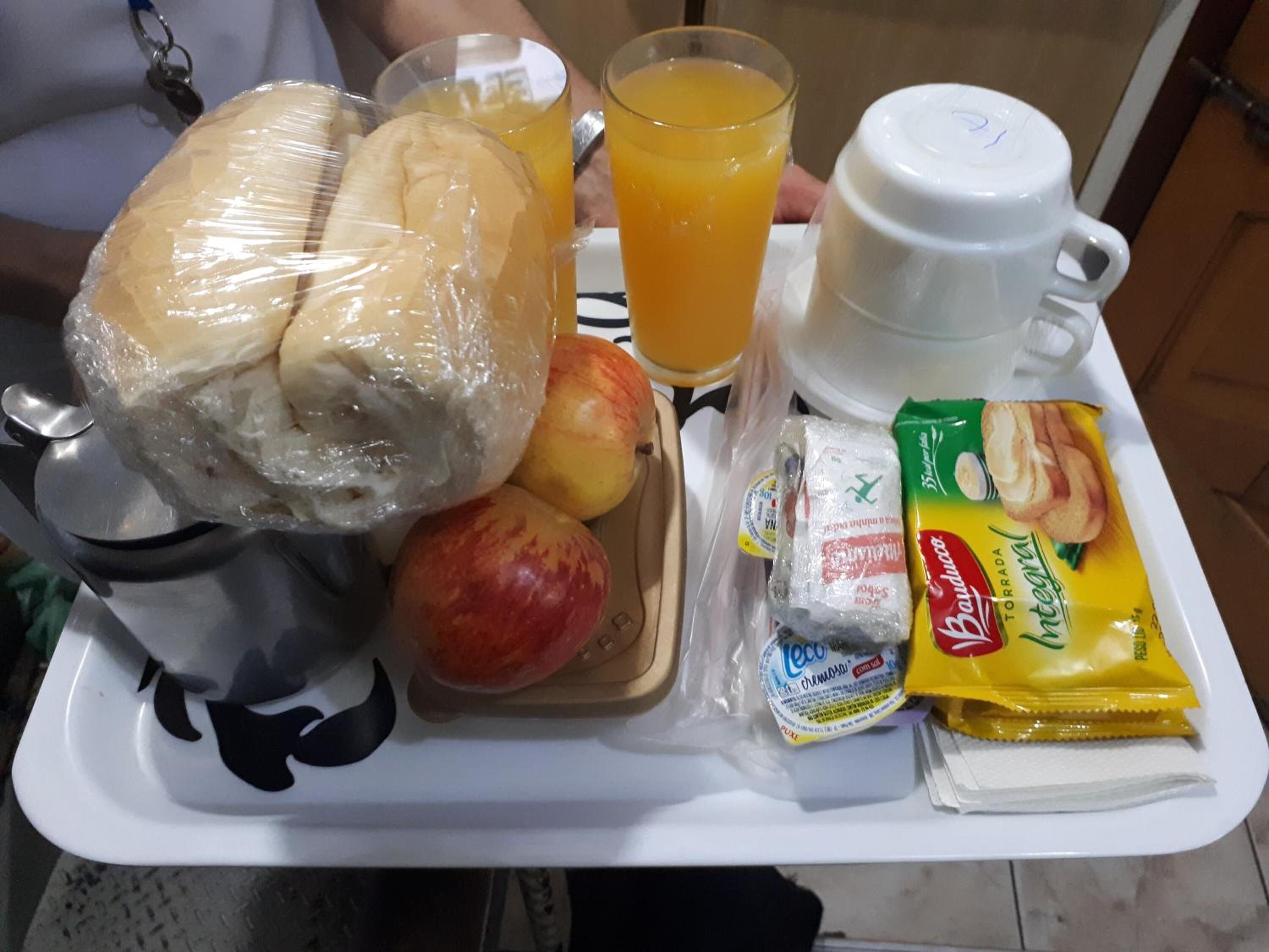 Uma bandeja de café da manhã com pão, maçãs, suco, iogurte e um saquinho de manteiga.