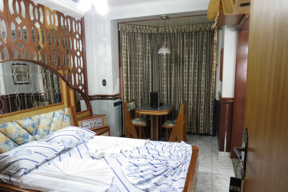 A hotel room with a bed, a desk, a chair, a curtain, and a door with a lock.
