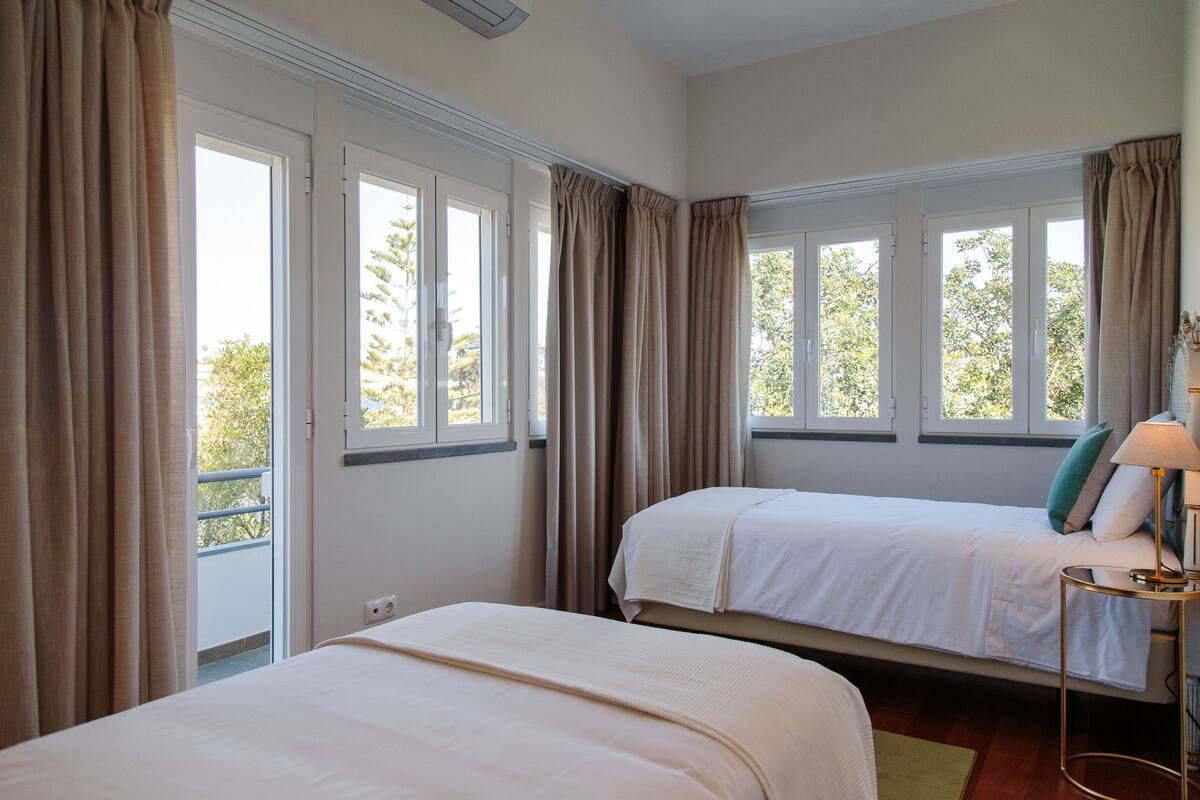 Une chambre d’hôtel avec deux lits, de grandes fenêtres et une vue sur les arbres.