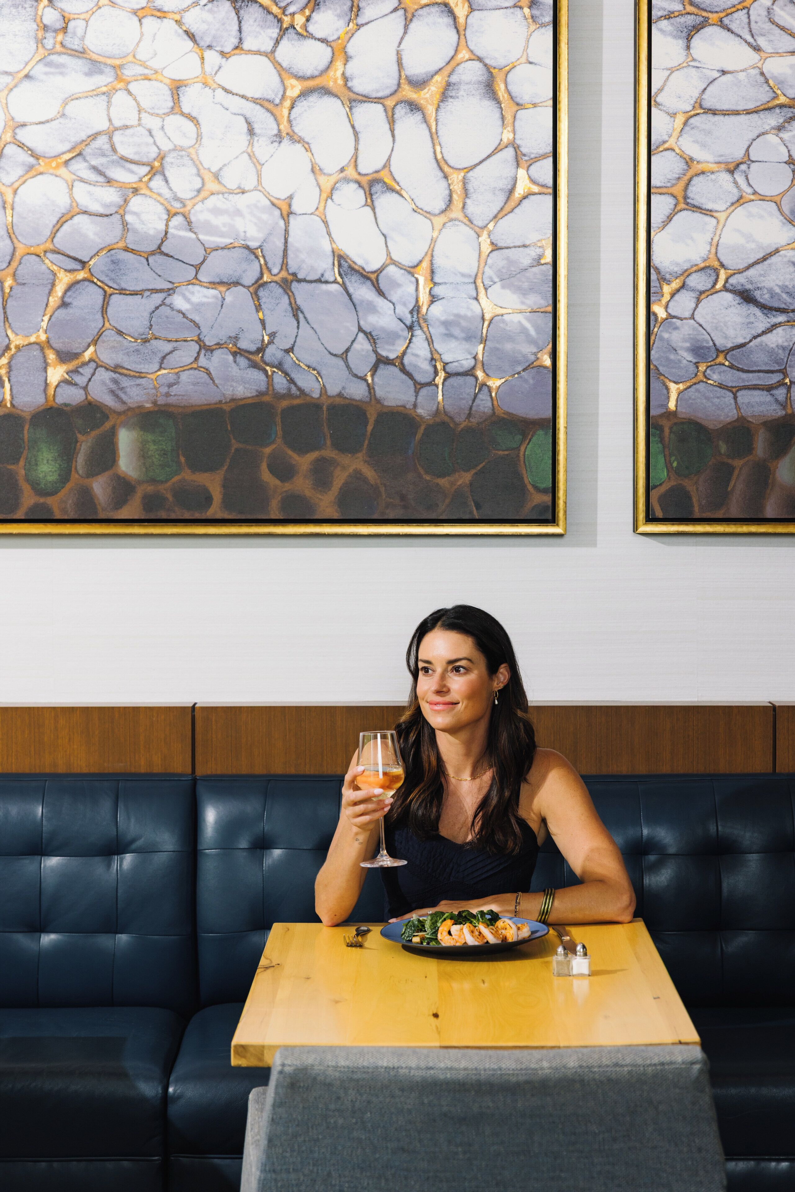 A person seated at a table with a plate of food and a glass of drink, in a room with a stone-patterned wall and a wooden panel.