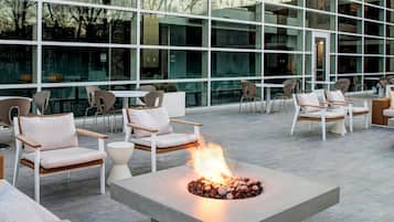 An outdoor seating area with a fire feature, modern furniture, and a large glass building in the background.