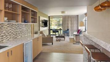 A modern kitchen with a tiled backsplash, wooden cabinets, and a built-in refrigerator. There is a dining area with a table and chairs, and a large window with curtains.
