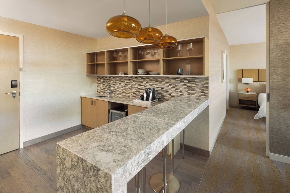 A modern kitchen with a marble countertop, wooden cabinets, and pendant lighting.