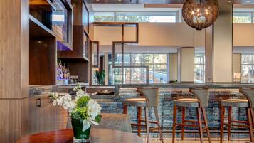 A modern bar area with wooden accents, bar stools, and a round table with a vase of flowers.
