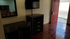 Een hotelkamer met een bureau, twee stoelen, een aan de muur bevestigde televisie en een rode deur naar buiten.