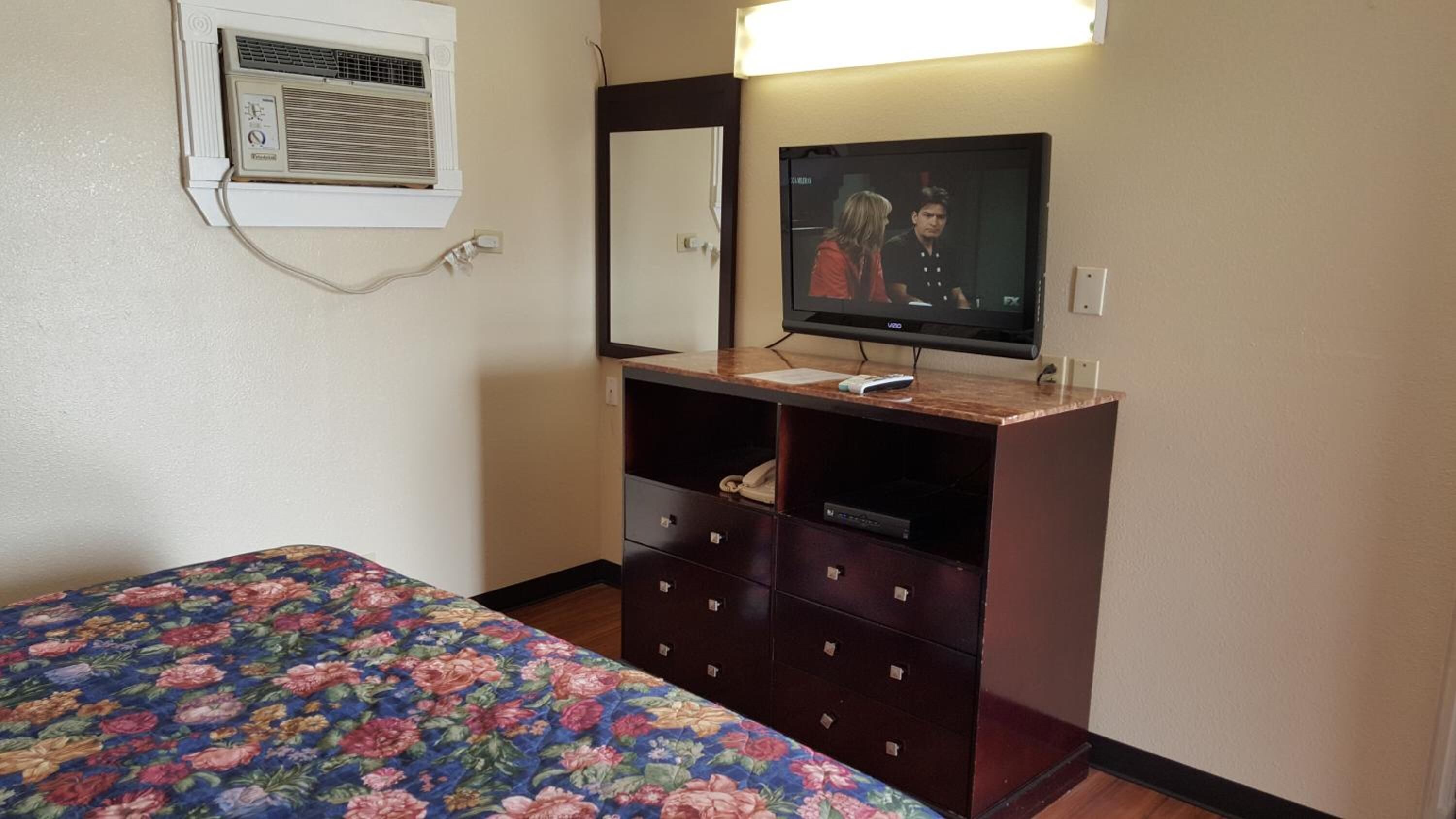 A hotel room with a bed, a dresser, a television, and an air conditioning unit.