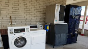 Een wasserette met een voorlader wasmachine en droger, een automaat en een afvalbak.