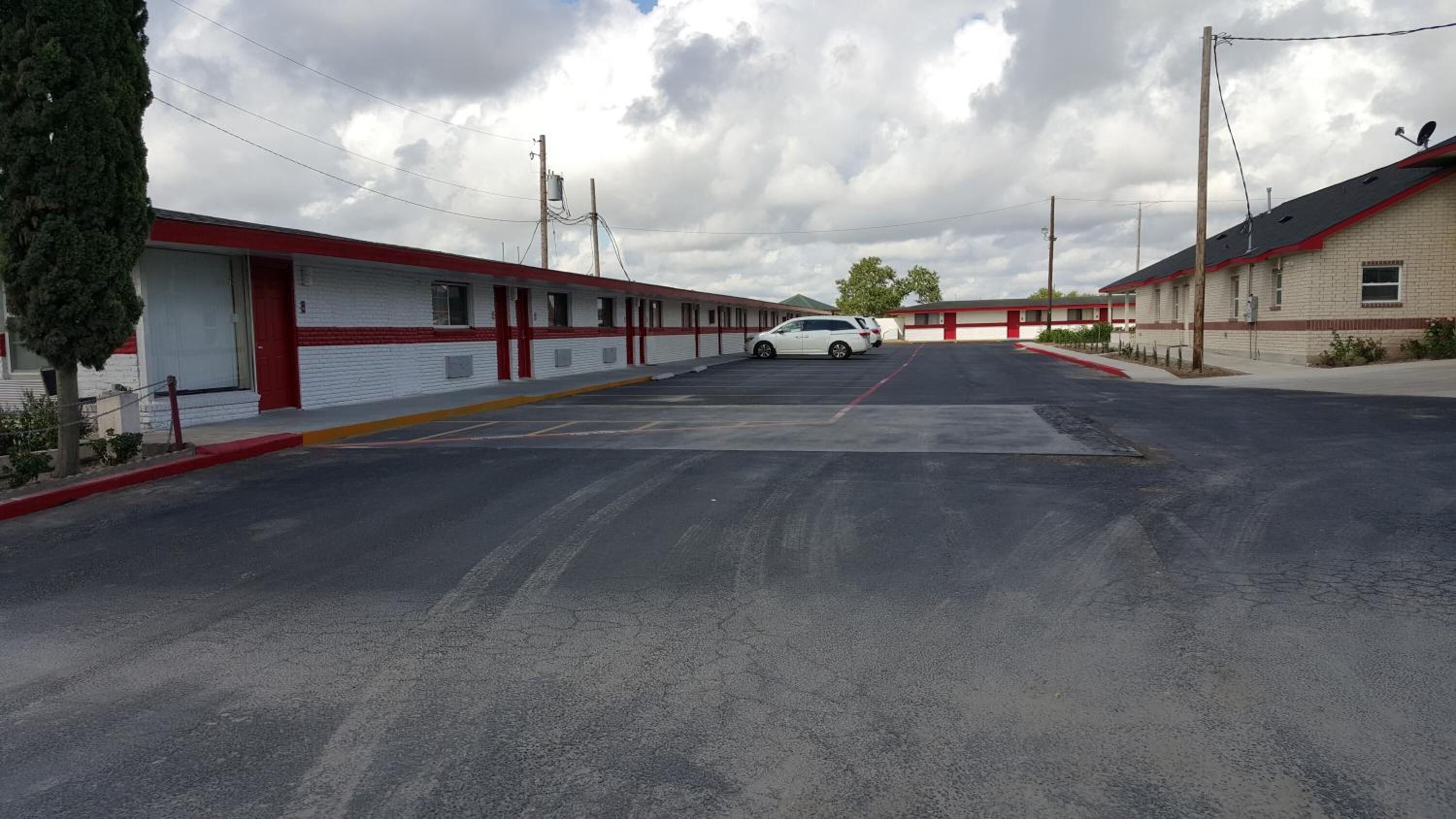 A motel with a row of single-story buildings, a parking lot, and a white car parked in the lot.