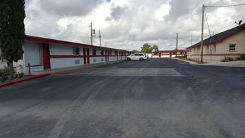 A motel with a row of single-story buildings, a parking lot, and a white car parked in the lot.