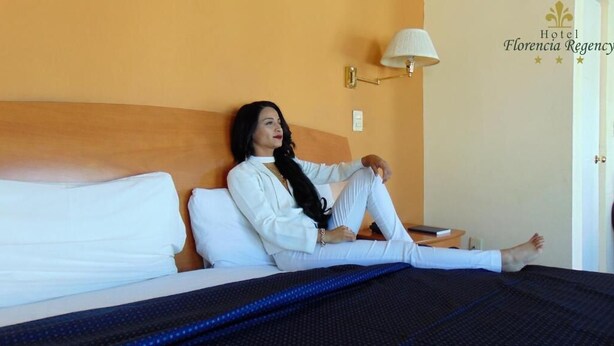 A hotel room with a bed, a nightstand, and a wall-mounted lamp.