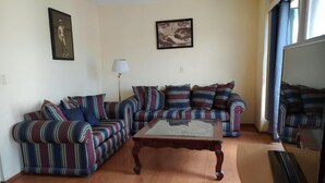 A living room with a striped sofa set, a glass-top coffee table, and a television.