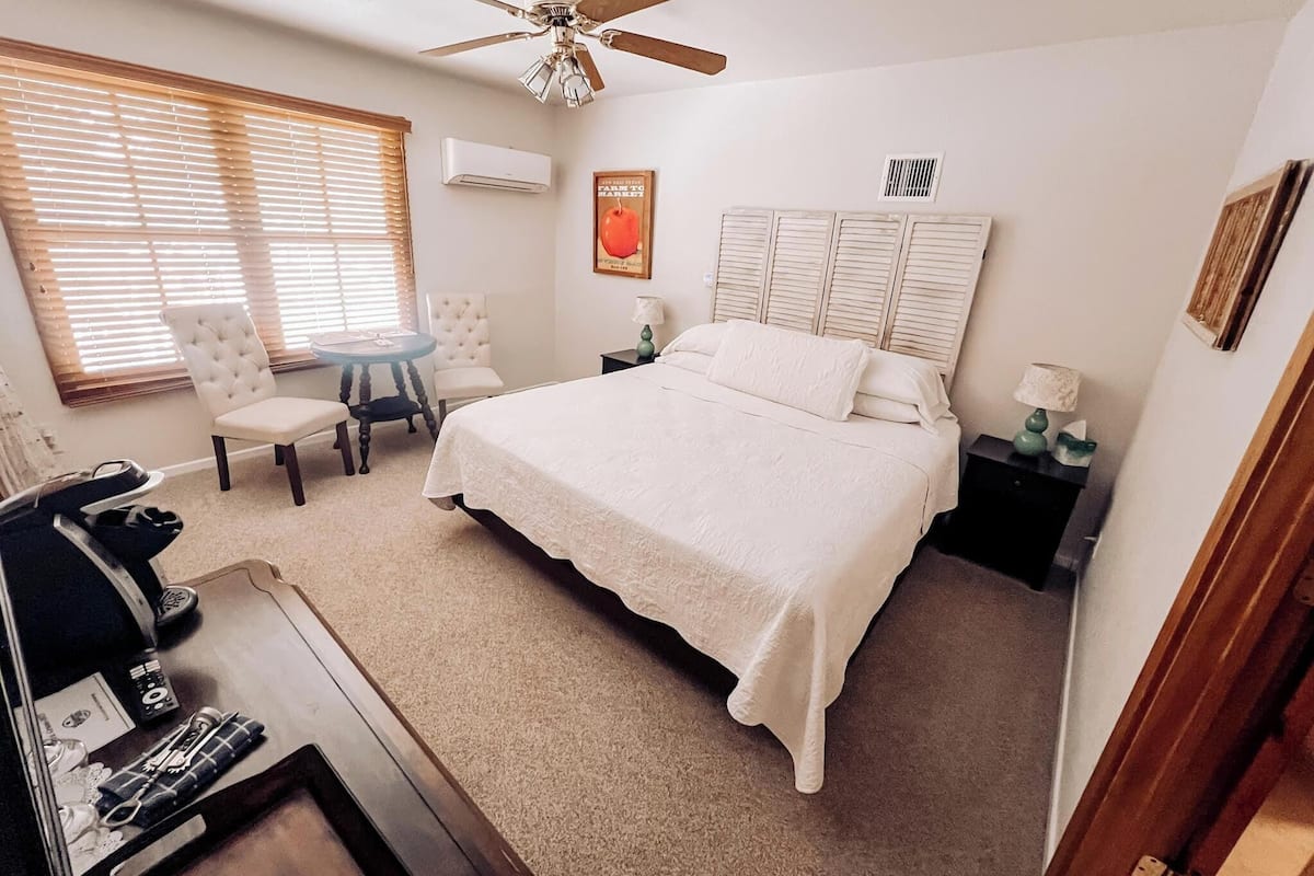 A bedroom with a bed, a chair, a desk, a ceiling fan, and a window with blinds.