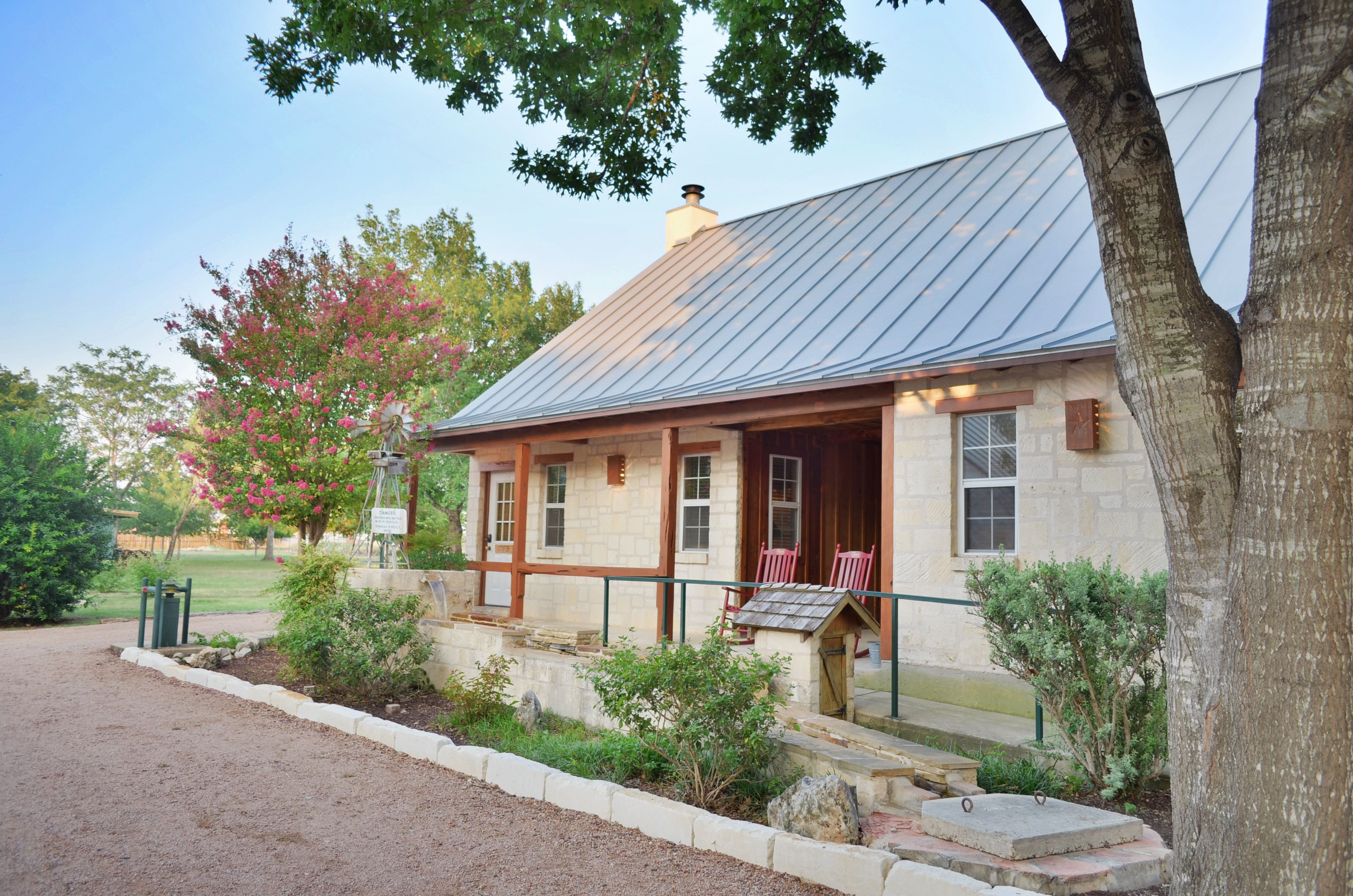 A stone building with a metal roof, a porch with red chairs, and a well-maintained garden.