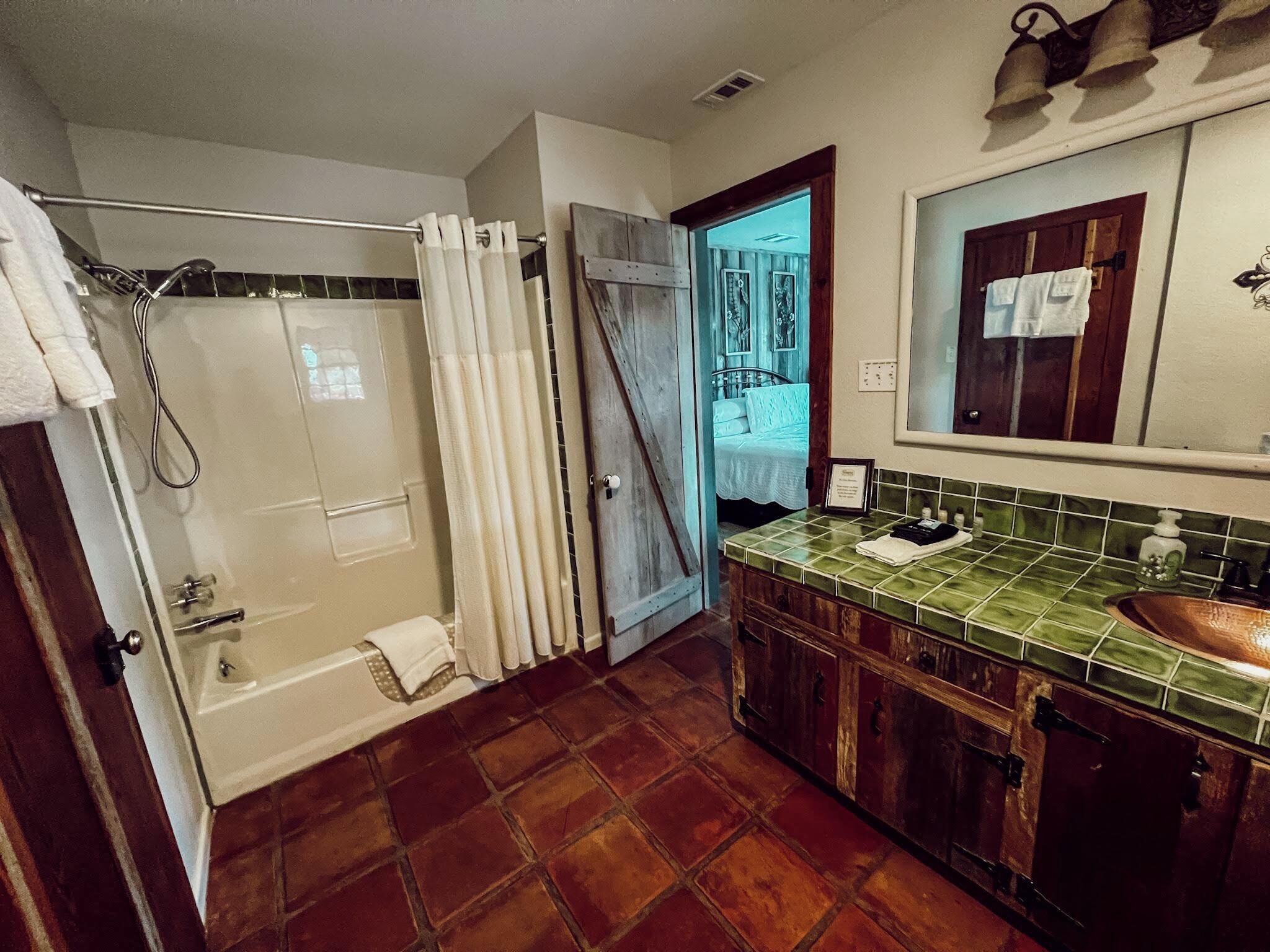 Un baño con ducha, bañera, lavamanos con salpicadero de azulejos verdes y un armario de madera.