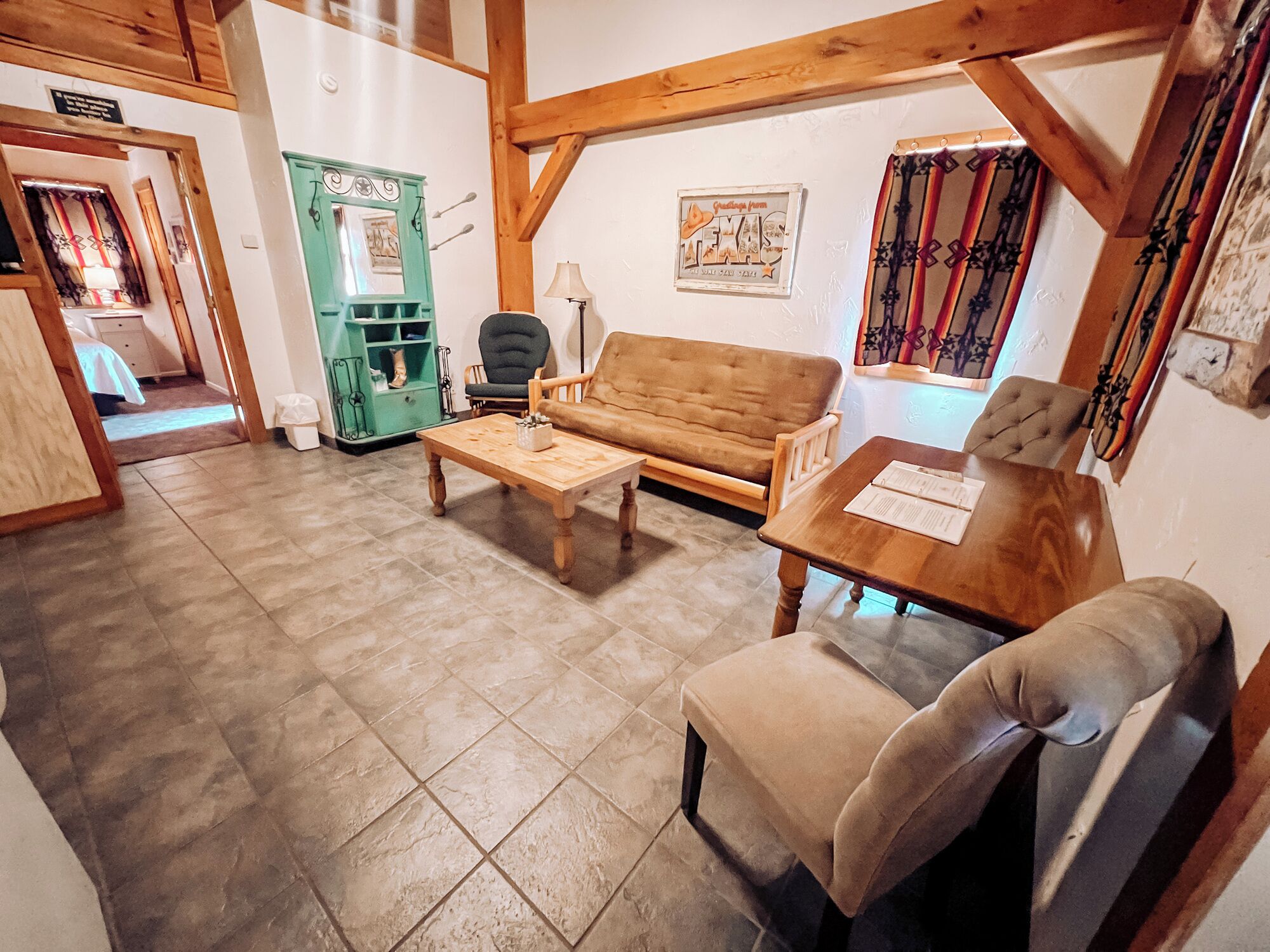 Una sala de estar acogedora con una mesa de centro de madera, un sofá y un sillón. Hay un armario verde y una puerta con un letrero.