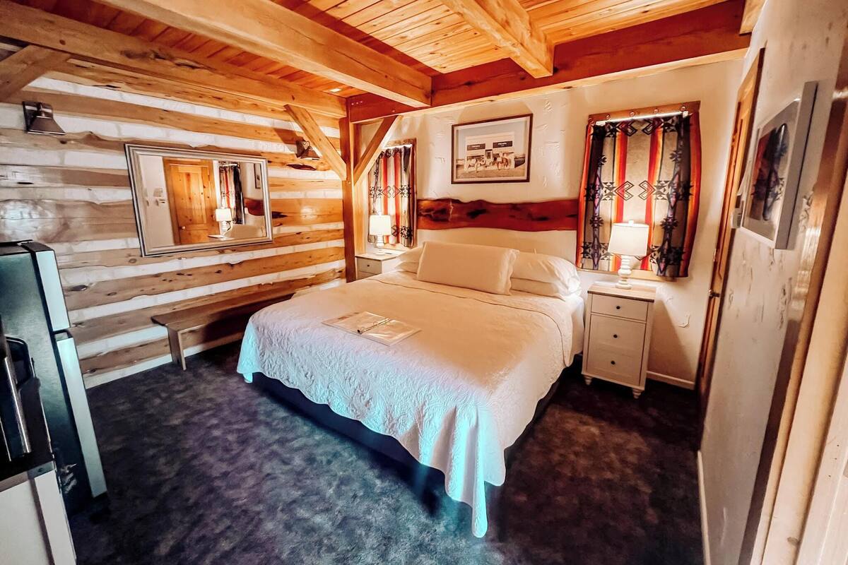 A log cabin-style bedroom with a bed, bedside tables, a mirror, and a picture on the wall.