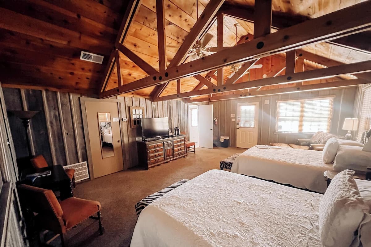 A spacious room with two beds, a television, and a dresser.