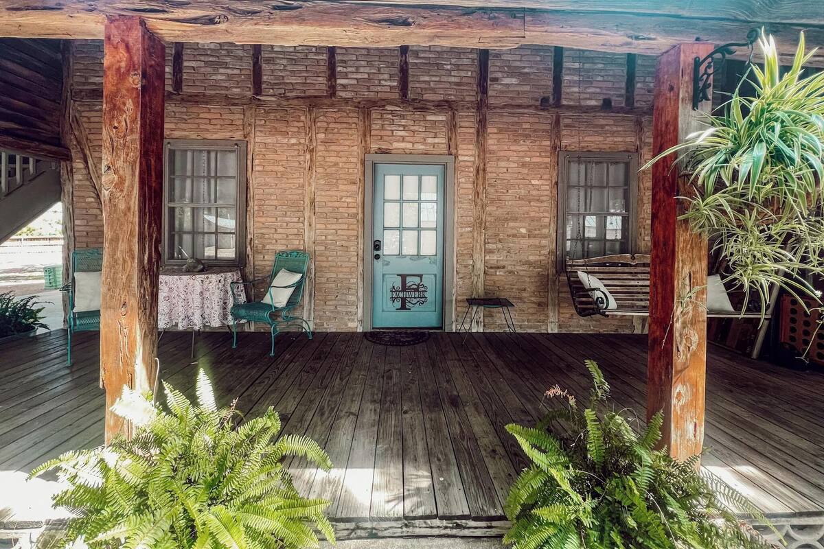 A wooden porch with a door, two windows, a chair, and a swing.