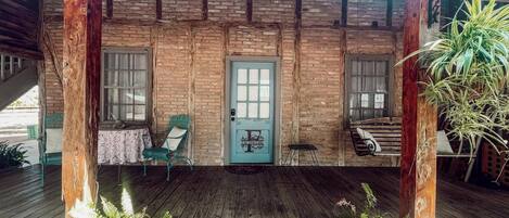 A wooden porch with a door, two windows, a chair, and a swing.