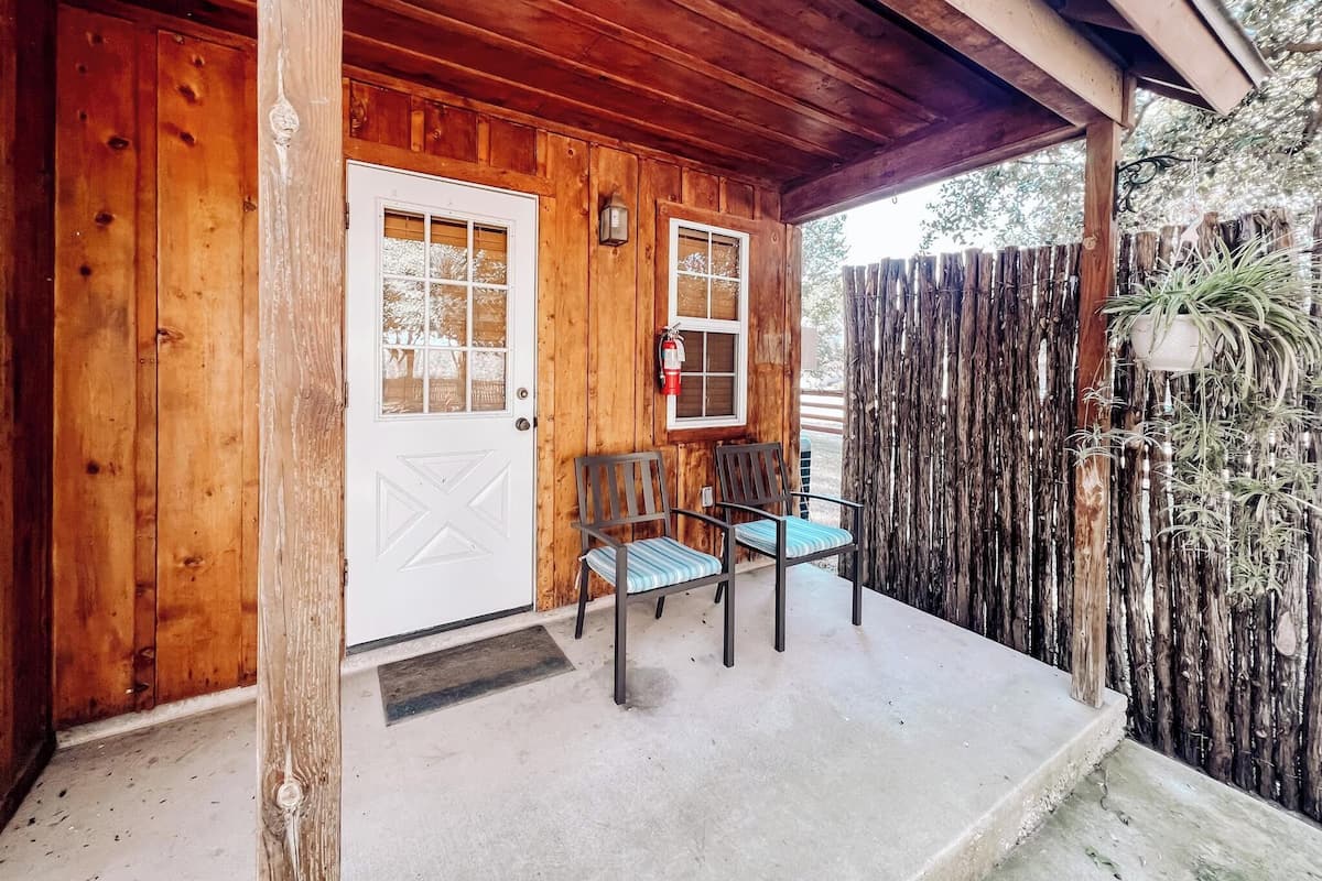 A wooden cabin with a porch, a white door, and two chairs.