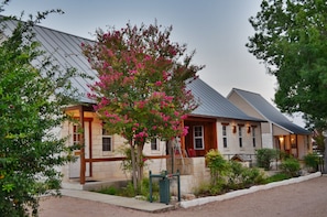 A stone building with a metal roof, surrounded by greenery and a tree with pink flowers. - Gruene Cottages (New Braunfels)