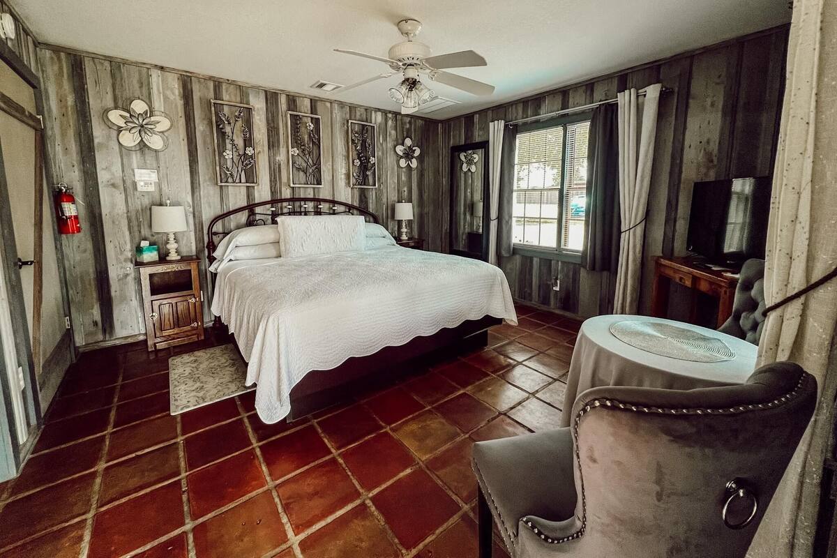 A bedroom with a bed, a chair, a television, and a ceiling fan.
