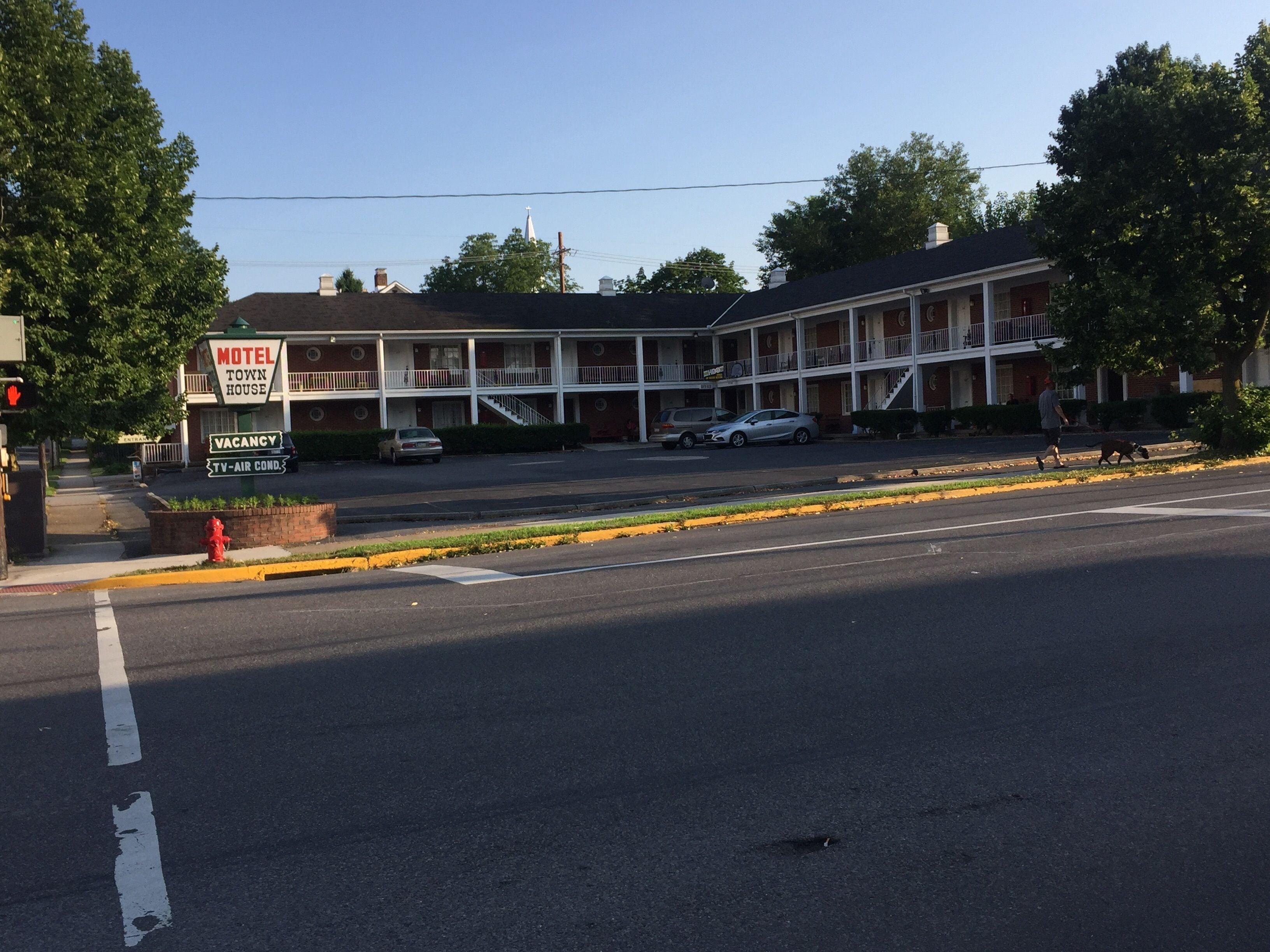 A motel with a two-story structure, a covered parking area, and a fire hydrant on the sidewalk.