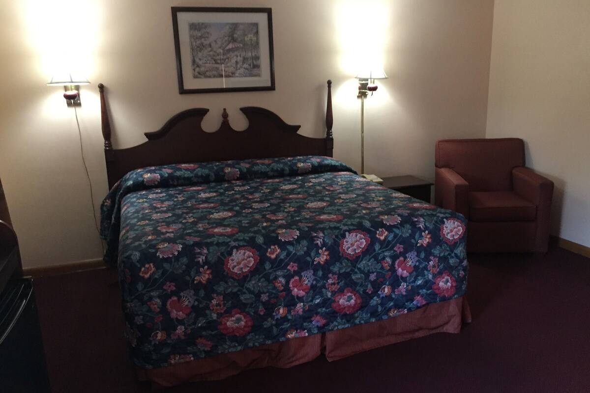 A hotel room with a bed, two wall-mounted lamps, a chair, and a framed picture on the wall.