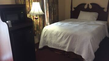 A hotel room with a bed, a desk with a lamp, and a television.