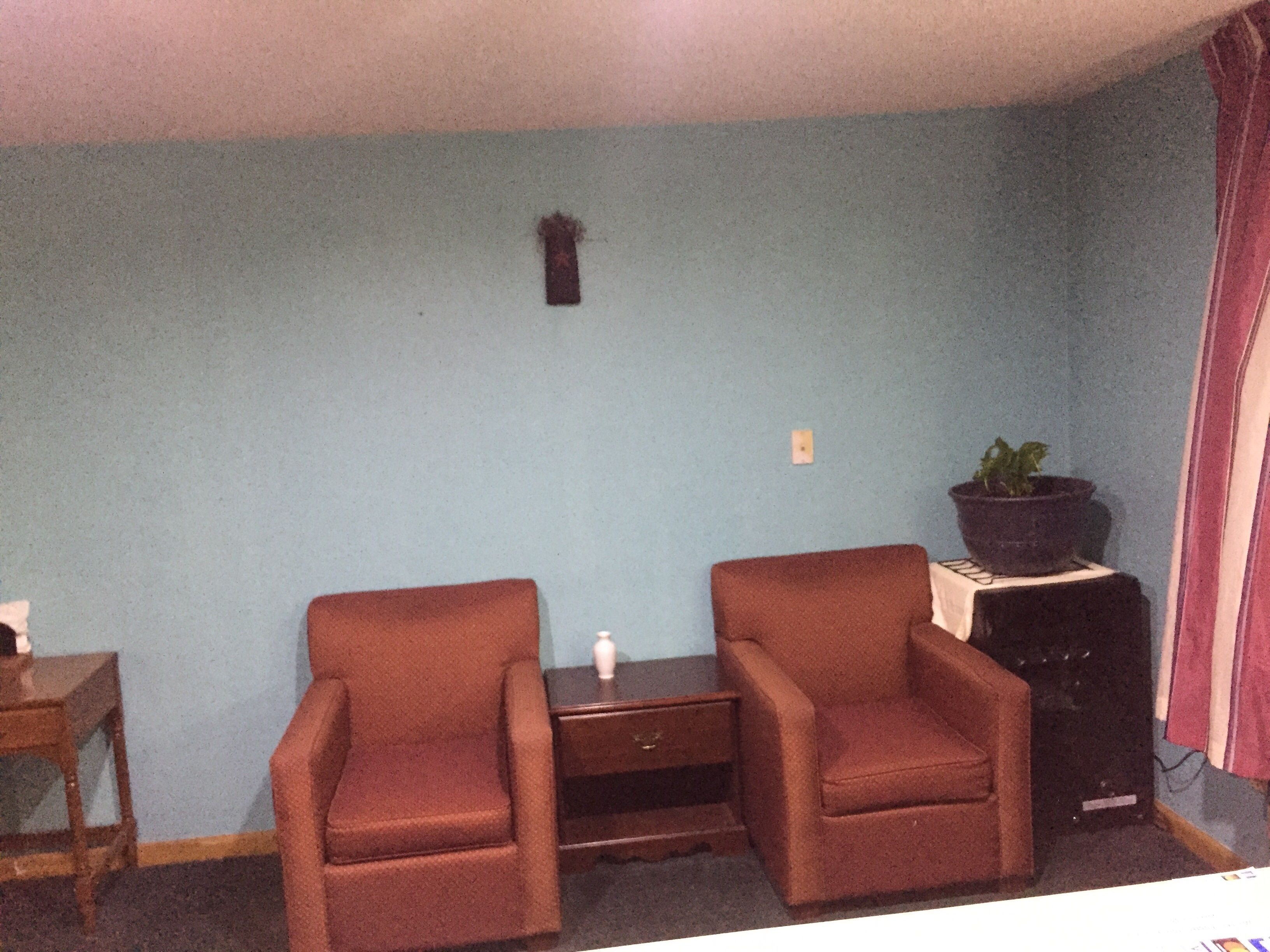 A room with two brown armchairs, a small table, a potted plant, and a dark-colored cabinet.