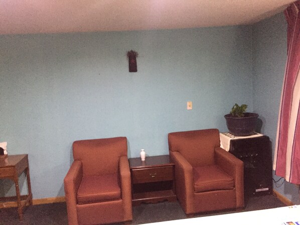 A room with two brown armchairs, a small table, a potted plant, and a dark-colored cabinet. - Motel Townhouse (Bedford)
