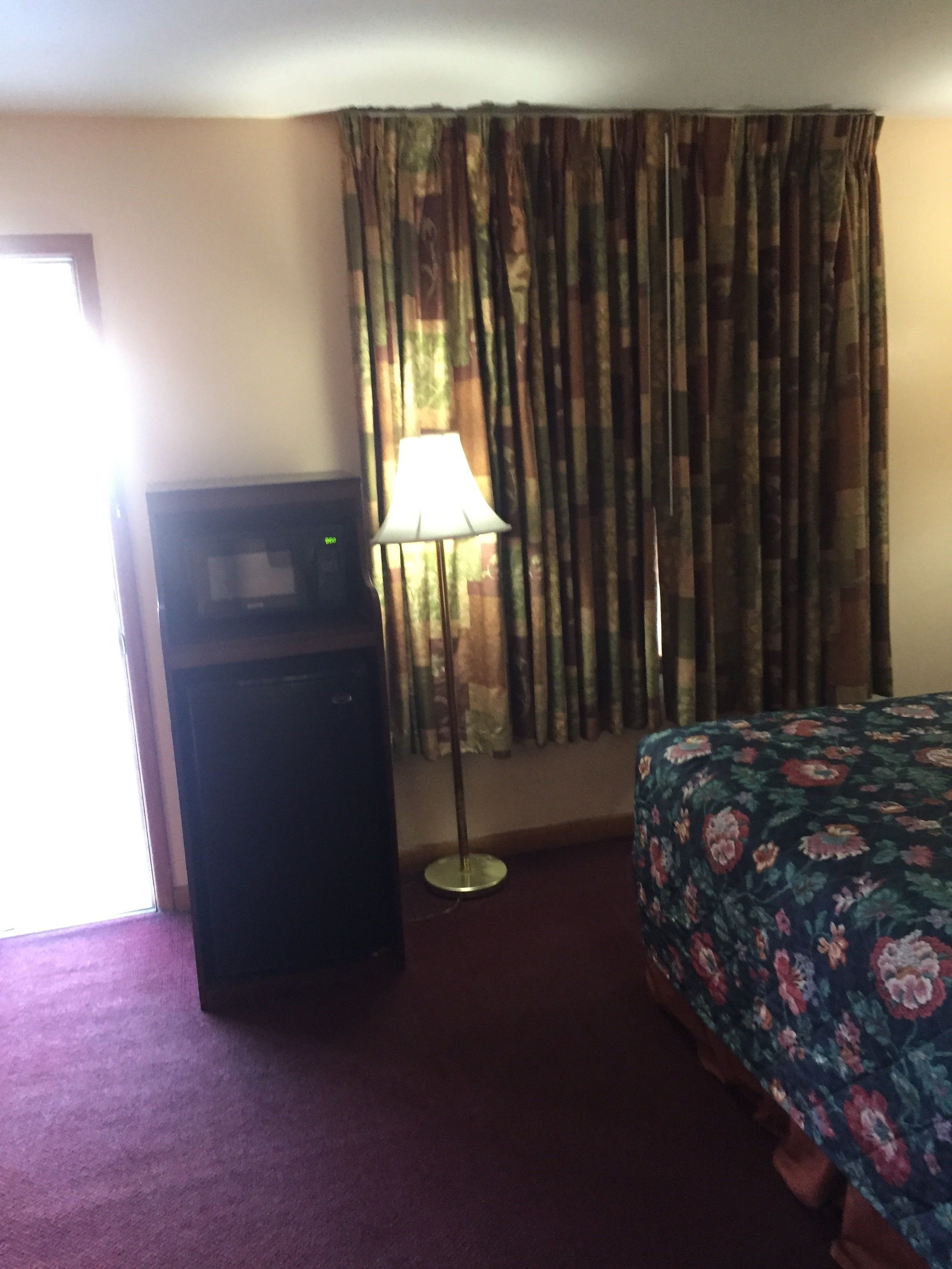 A hotel room with a bed, a desk, a lamp, and curtains.