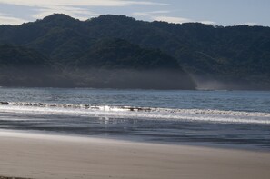 A beach with waves, a sandy shore, and a forested hill in the background. - Viva Tambor Villas (Paquera)