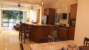 A modern kitchen with wooden cabinets, a large island, and a dining area with a table set for four. - Viva Tambor Villas (Paquera)