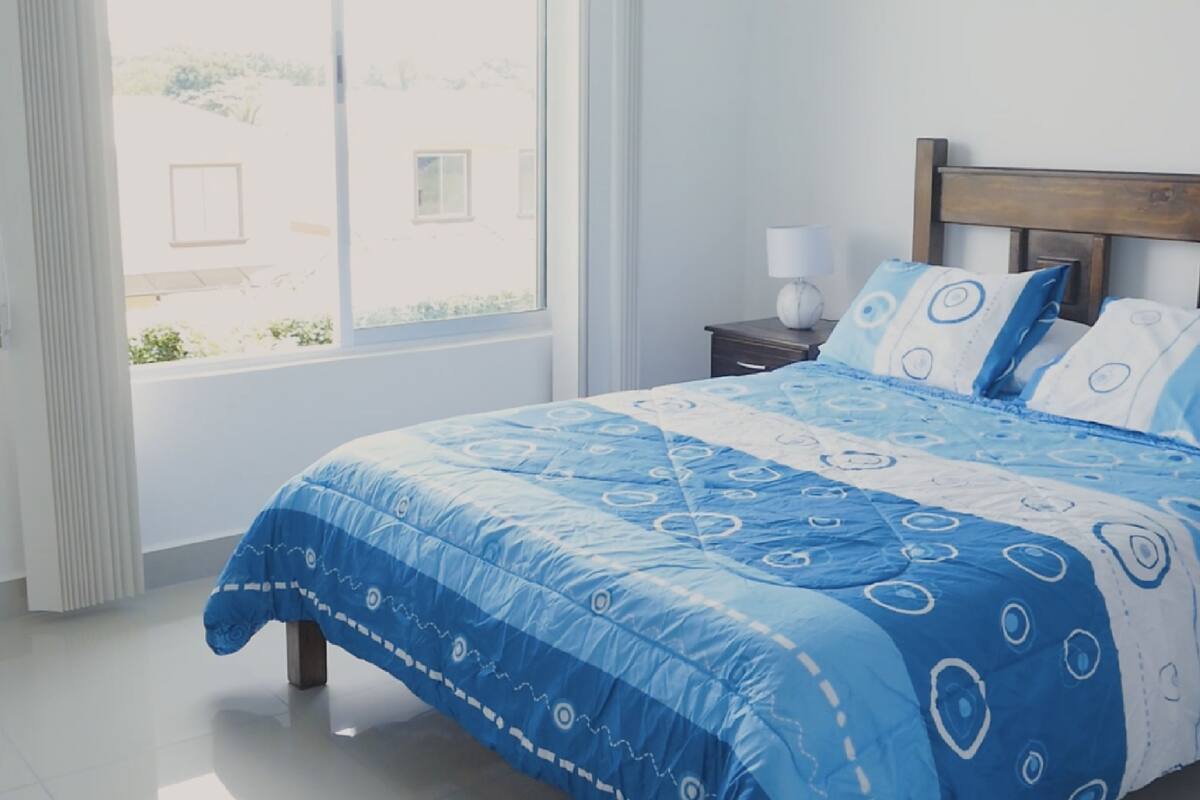 A bedroom with a bed, a nightstand, a lamp, and a window with a view of buildings.