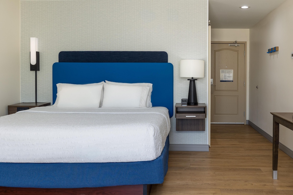 A hotel room with a bed, bedside tables, a lamp, a nightstand, and a door.