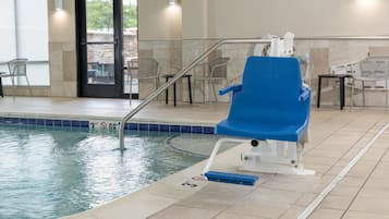 An indoor swimming pool with a blue pool chair, a pool ladder, and a no diving sign.