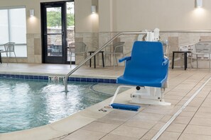 Une piscine intérieure avec une chaise bleue au bord du bassin, un escalier pour y accéder et un panneau indiquant qu’il est interdit de plonger.
