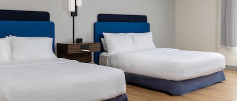 A hotel room with two beds, a nightstand, a lamp, and a window with curtains.