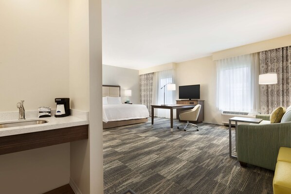 A hotel room with a bed, desk, chair, sofa, and a small kitchenette area. - Hampton Inn & Suites Niles/Warren (Niles)