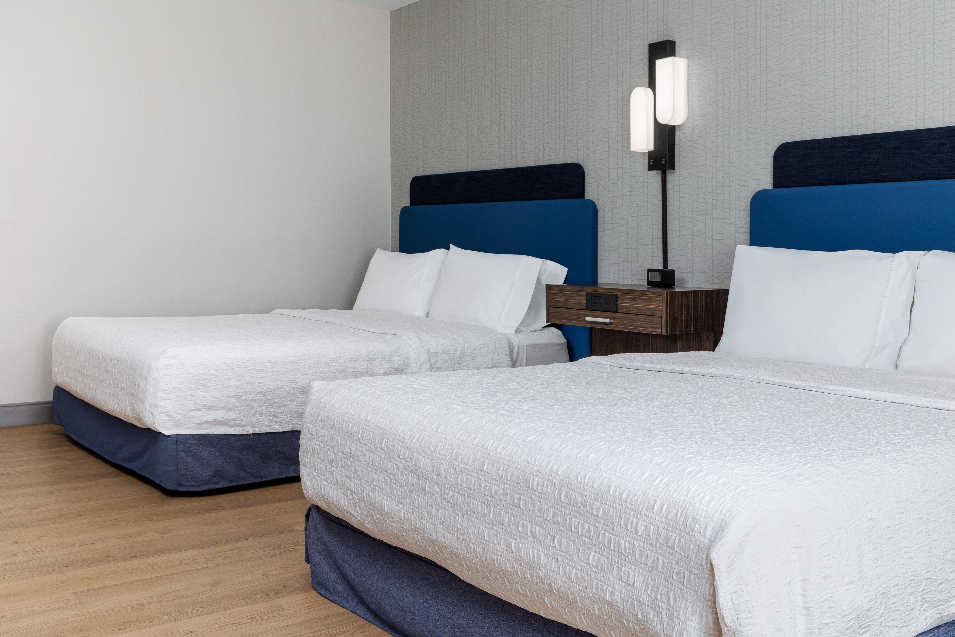 A hotel room with two beds, a nightstand, and a wall-mounted lamp.