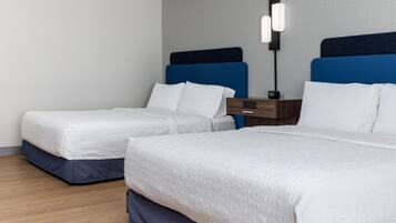 A hotel room with two beds, a nightstand, and a wall-mounted lamp.