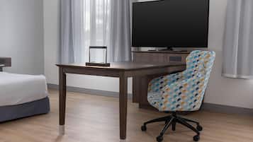 Ett hotellrum med en säng, ett skrivbord, en stol, en tv och gardiner.
