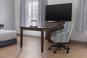 Habitación de hotel con cama, escritorio, silla, televisor y cortinas.