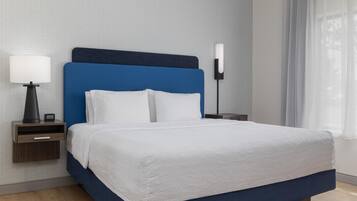 Ein ordentlich bezogenes Bett mit weißer Daunendecke, einem blauen Kopfteil und einer Nachttischlampe auf einem Holznachttisch.