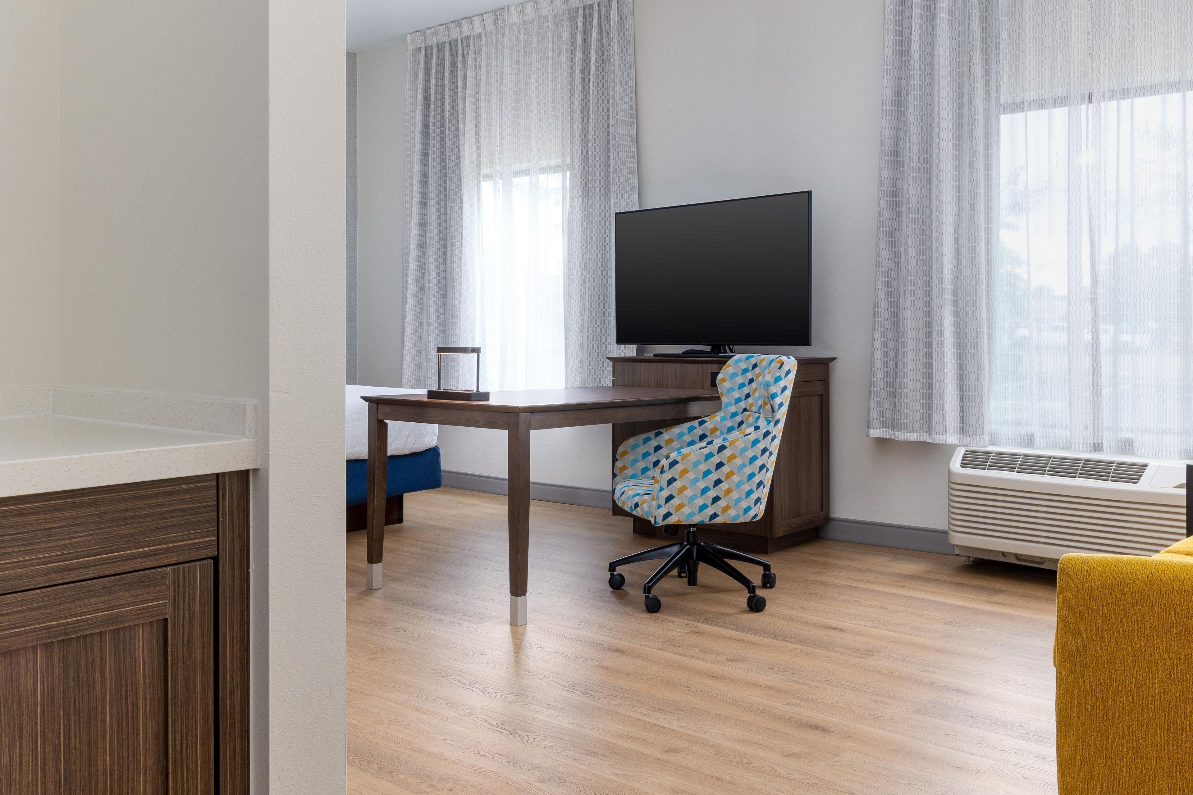 A room with a wooden desk, a chair, a television, and an air conditioning unit.
