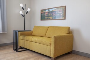 Un sofá color mostaza con estructura metálica negra, ubicado frente a una pared con un cuadro enmarcado encima.